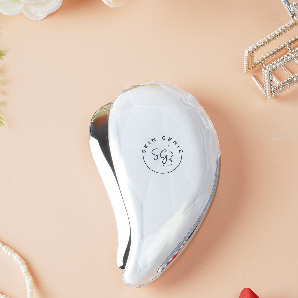 The electric gua sha on a dressing table with pearls and a lipstick